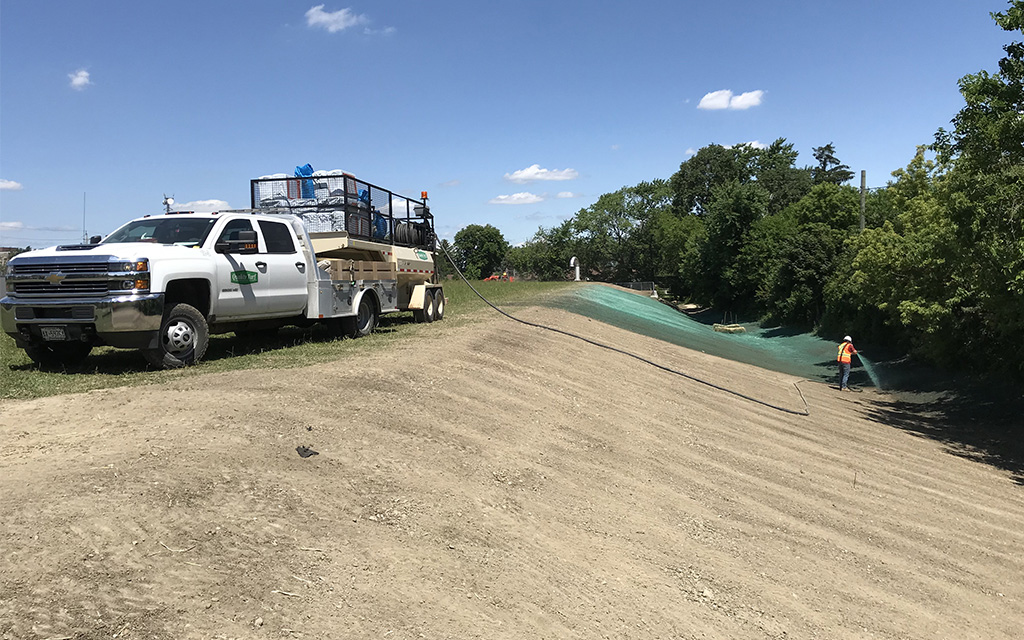 Quality Turf crew member applying green hydroseed mulch to a large sloped hillside from a professional hydroseeding truck to prevent erosion and grow new grass.