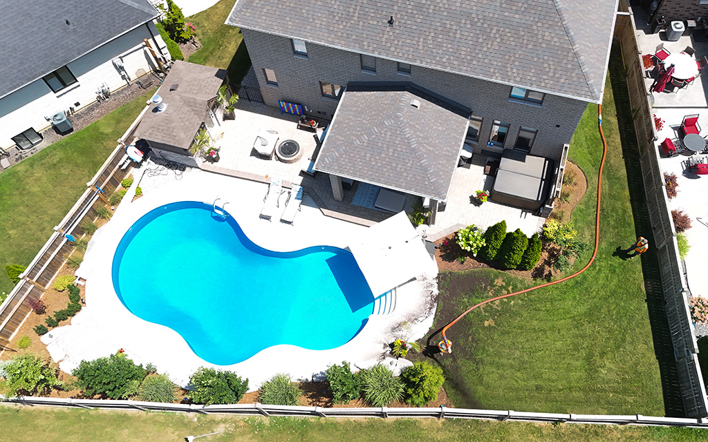 Aerial drone view of Quality Turf blower truck hose navigating around a residential swimming pool and tight backyard fence line to spread landscaping material.