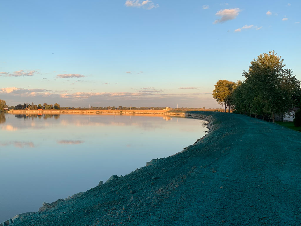 A curved, newly hydroseeded green shoreline bank running alongside a body of water.