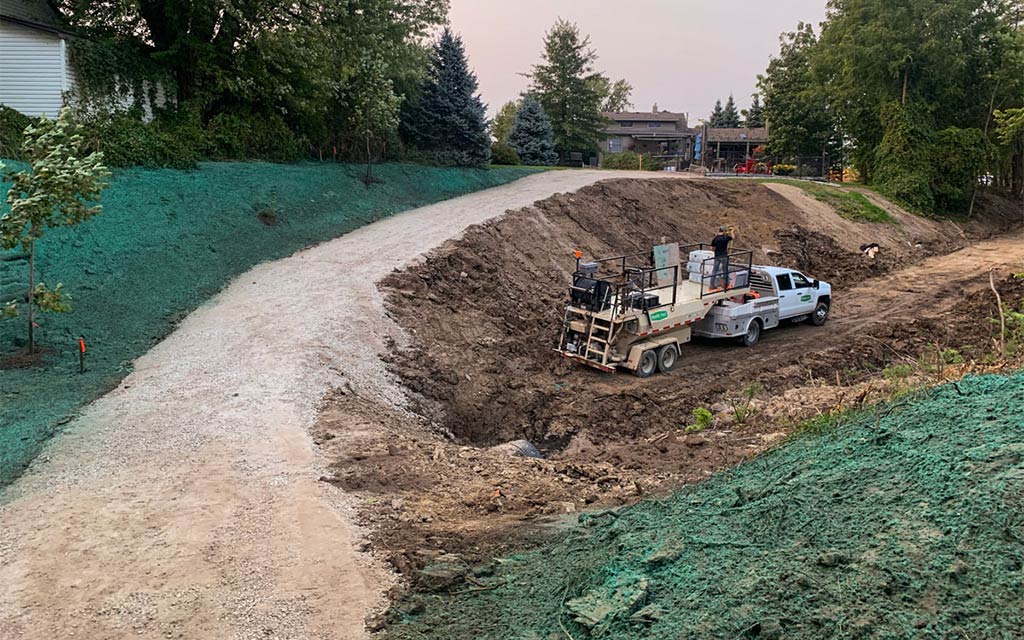 A hydroseeding truck parked beside a freshly graded dirt road and hydroseeded green slopes.