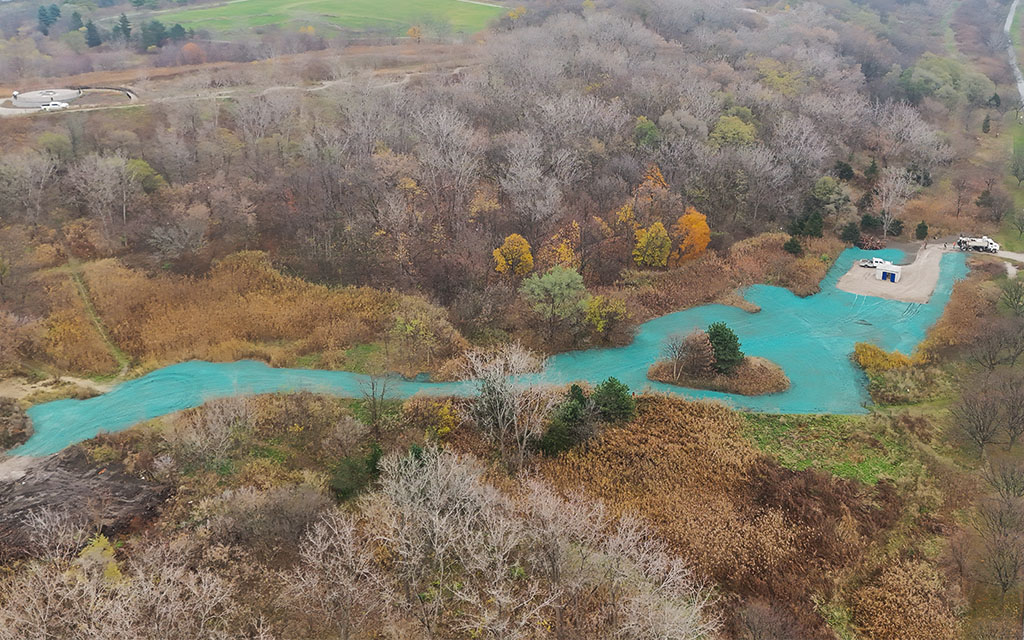 High-angle aerial view of a winding natural channel and landscape site treated with green hydroseed mulch during autumn.