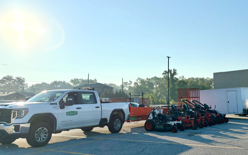Commercial landscaping truck and trailer loaded with professional lawn care mowers and equipment.